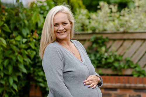 Anne-Marie standing in her garden, with her hands on her baby bump. She is smiling.