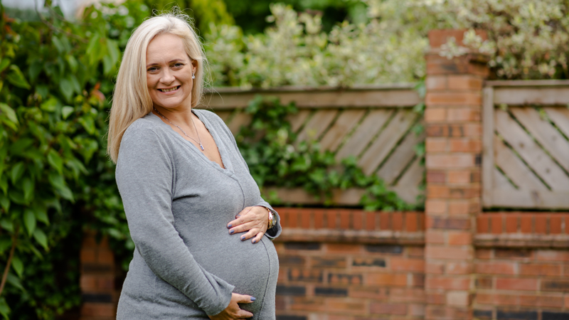 Anne-Marie standing in her garden, with her hands on her baby bump. She is smiling.