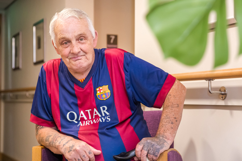 Chris sitting in a chair, leaning slightly forward. He is wearing a Barcelona football shirt