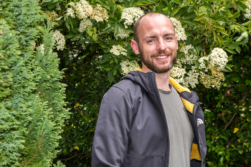 Philip F looking relaxed, standing in a garden, he is smiling.